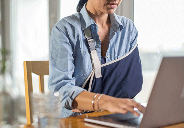 A woman working at a computer with a sling on one arm.